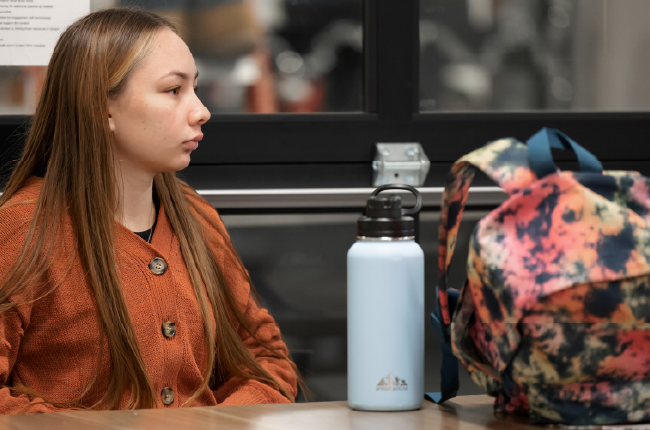 Student sitting at a desk with water bottle and backpack.
