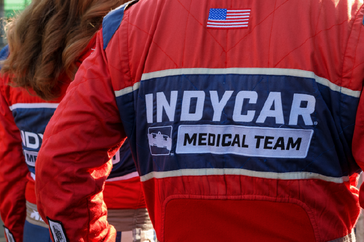 The backside of a red and blue Indy Car road racing suit is show, with text that reads Indycar Medical Team displayed in large white letters.