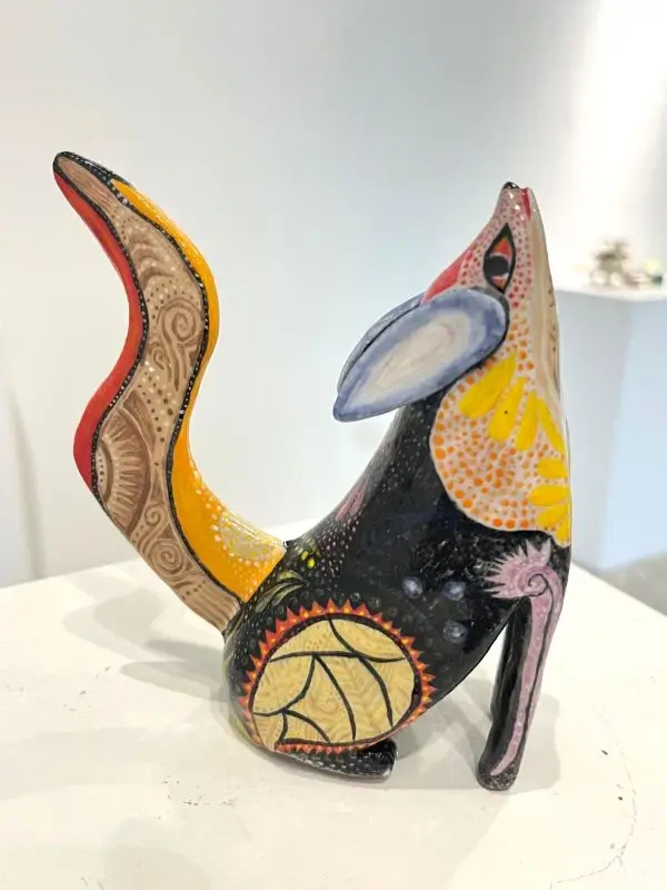 Colorful ceramic sculpture of a stylized fox-like creature with intricate painted patterns in yellow, red, black, and beige.