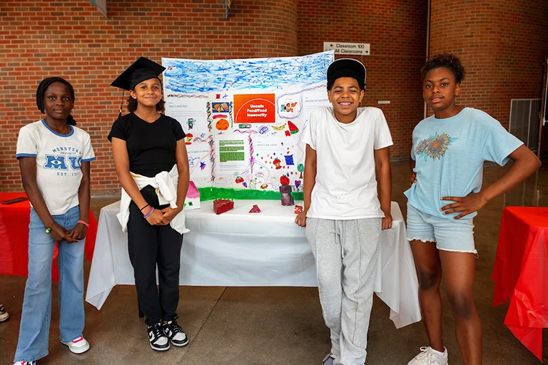 Four summer camp participants stand next to their presentation poster
