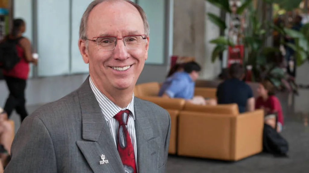 Chancellor Charles Bantz stands in a suit as students walk and gather behind him the the Campus Center.