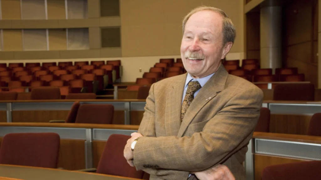 Chancellor Gerald Bepko stands in a suit, arms crossed, in front of an empty lecture hall.