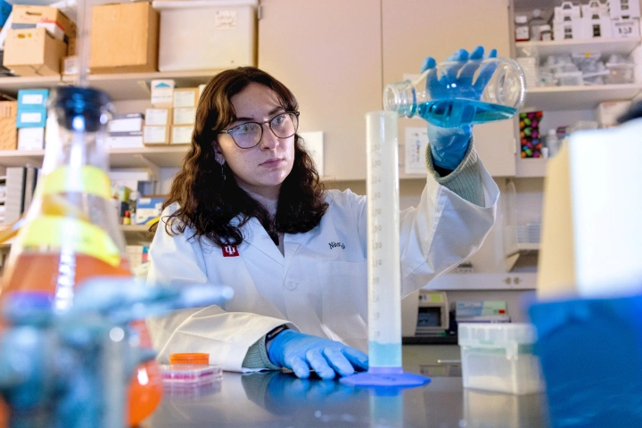 IU Indianapolis student, Maddie Lisenko, pours blue liquid into a graduated cylinder in a research lab.