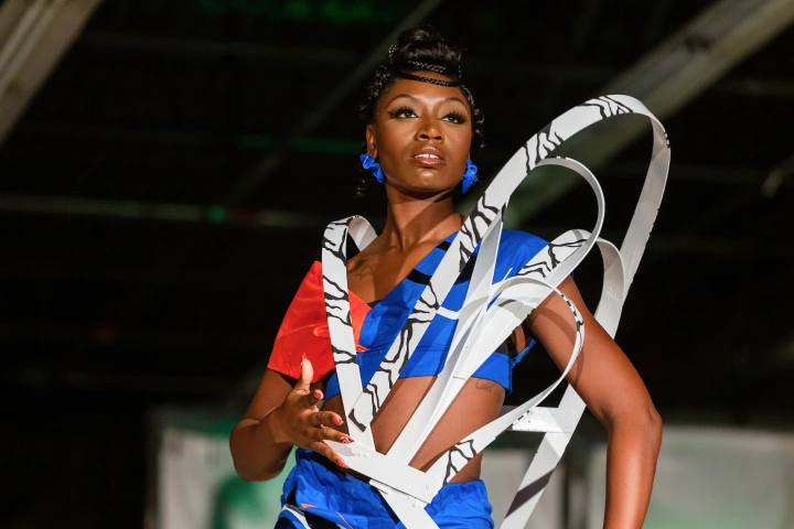 A woman in a blue and red outfit is encircled by a swooping white and black structure going around her waist and shoulders.