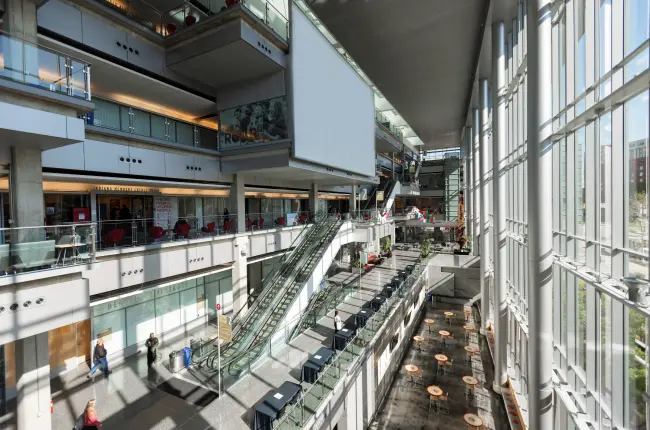 Bright, spacious atrium with multiple levels, escalators, glass railings, and floor-to-ceiling windows.