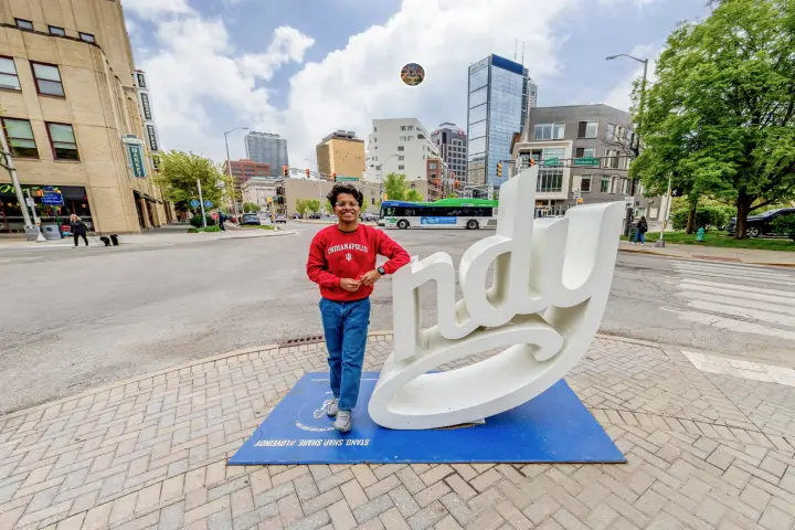 IU student standing next to the Indy sculpture downtown with city in background