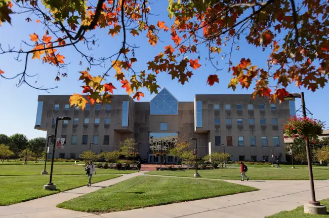 Modern university building framed by vibrant autumn leaves.