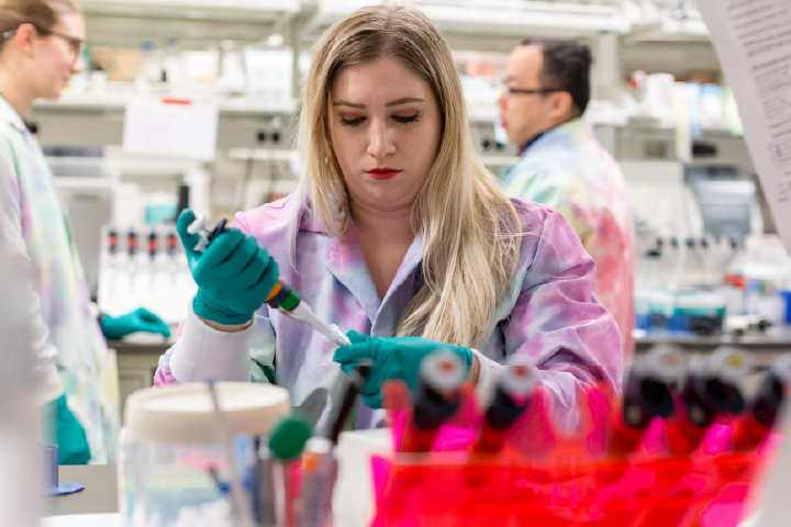 Student in multicolored lab coat using a pipet. 