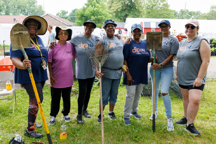 Group of individuals holding shovels and rakes at a local community garden.