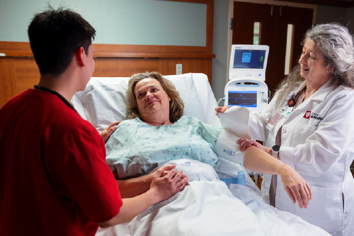Women in hospital bed looking at student nurse. Doctor is putting on a blood pressure cuff on woman.
