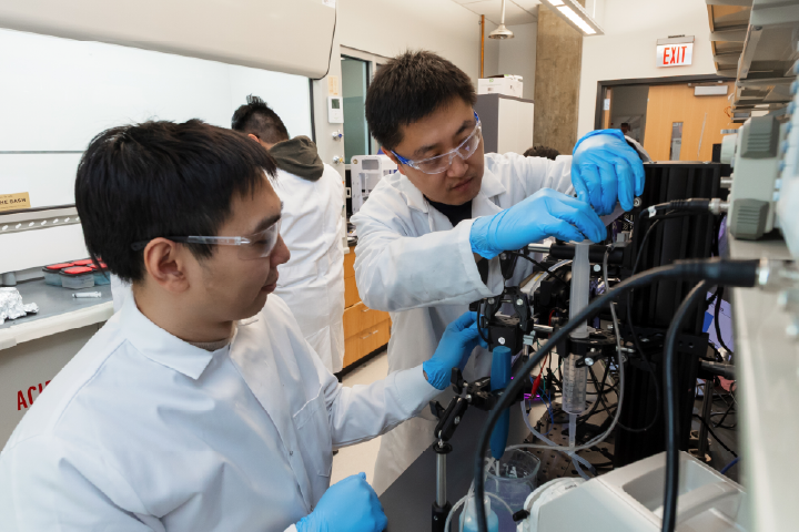 Two students wearing white lab coats working in a lab.