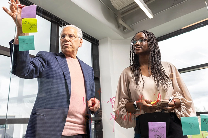 Dr. Richard DiMarchi places sticky notes on a glass wall while another person watches him.