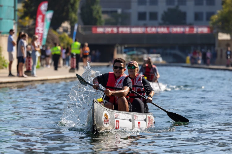 Two Regatta participants paddle a canoe, water splashing off their oars, through the downtown Indianapolis canal.