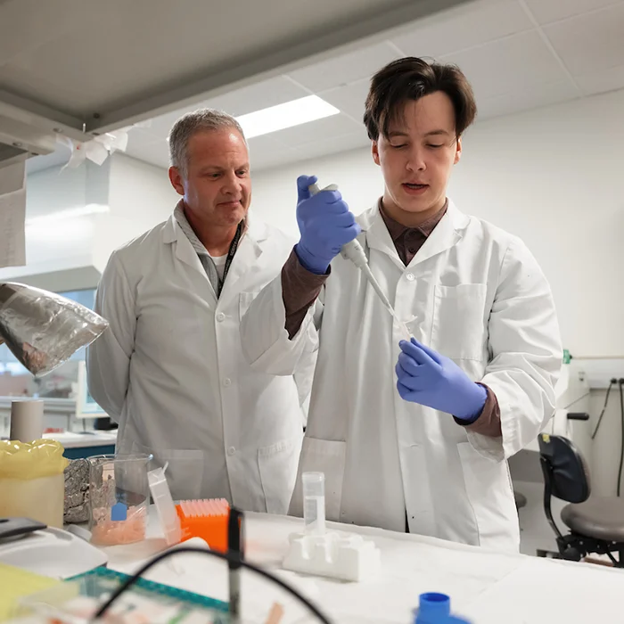 Person dropping liquid into test tube while another observes