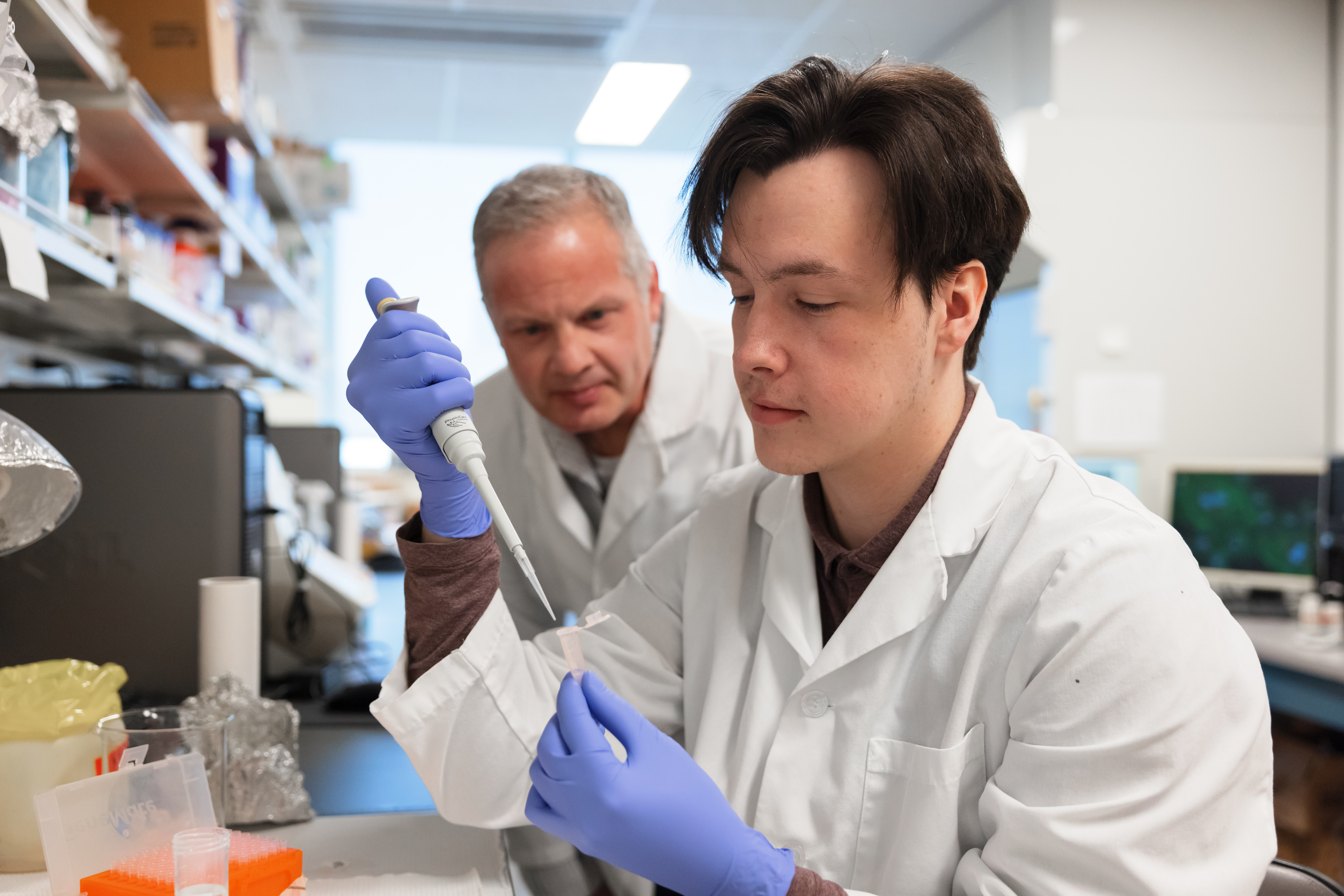 A student uses a pipette in a laboratory while a professor instructs them.