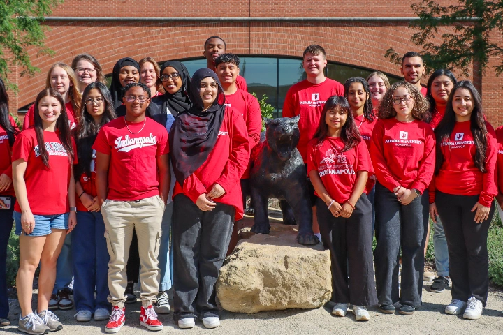 Students wearing red shirts gather around a jaguar statue.
