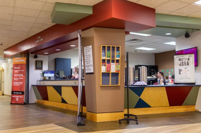 An open corner display of two service desks at the Bepko Learning Center, with two staff members seated behind public walk-up counters.