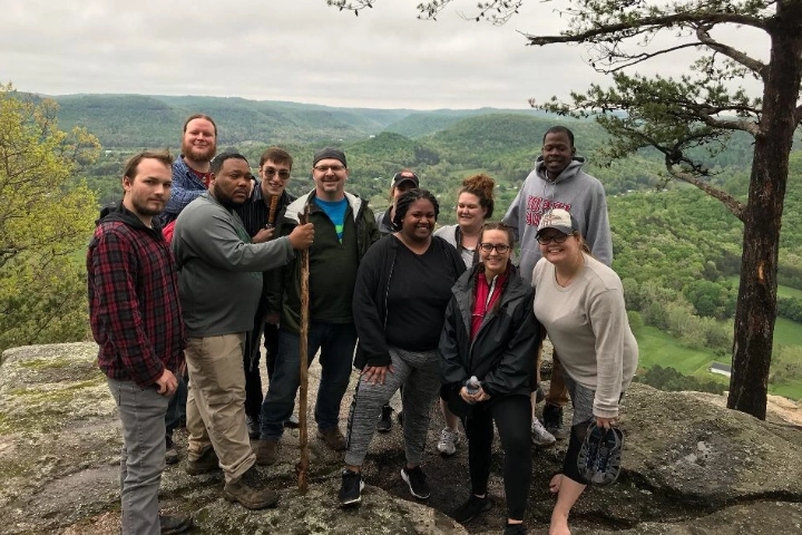 Students pose for a picture on a mountain. Behind them are green hills.