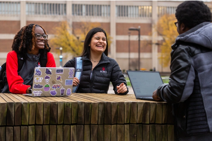 Students using laptops gather at an outdoor table.