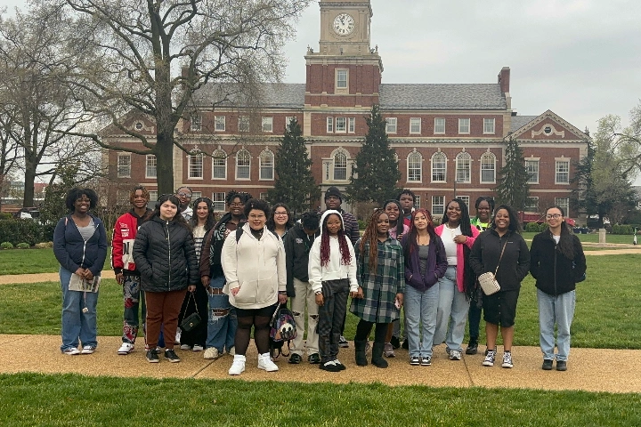 Upward Bound students pose for a picture in front of a large brick building with a clock tower.