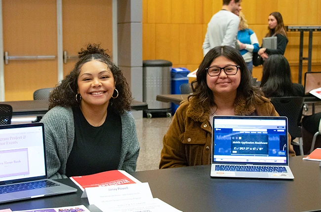 Two students smiling with presentations about their internship experience on a laptop in front of them