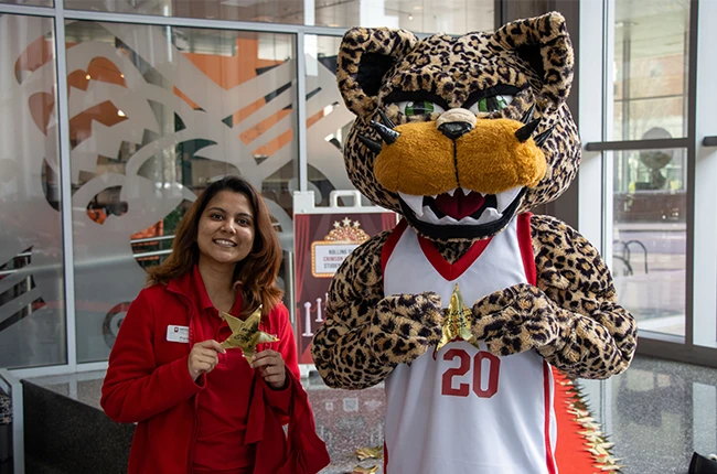 A student standing with a jaguar mascot both holding stars with their names on them