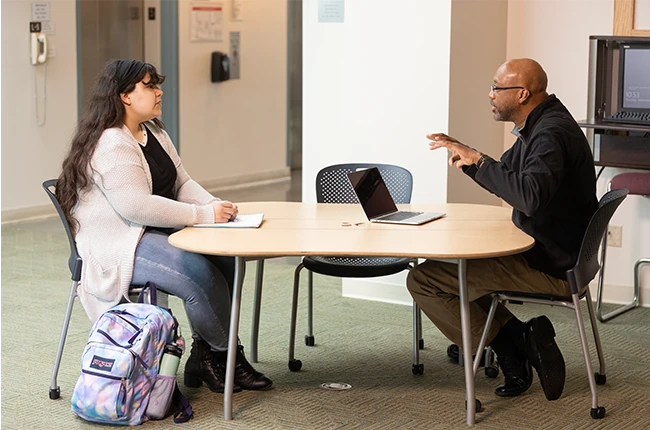 A student and an advisor sitting at a table and talking together
