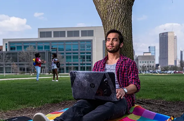 Student sitting outside under a tree with a laptop.