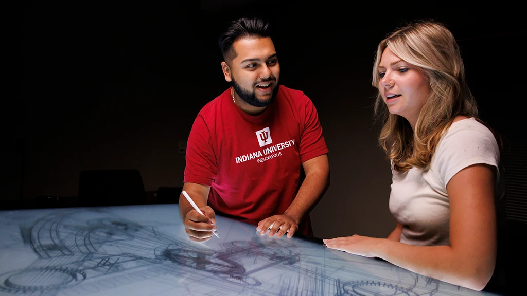 Two students sketching a diagram on a large touchscreen
