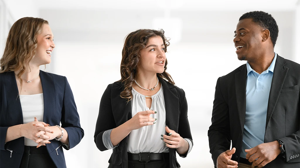 Three people in professional clothing talking in a brightly lit hallway