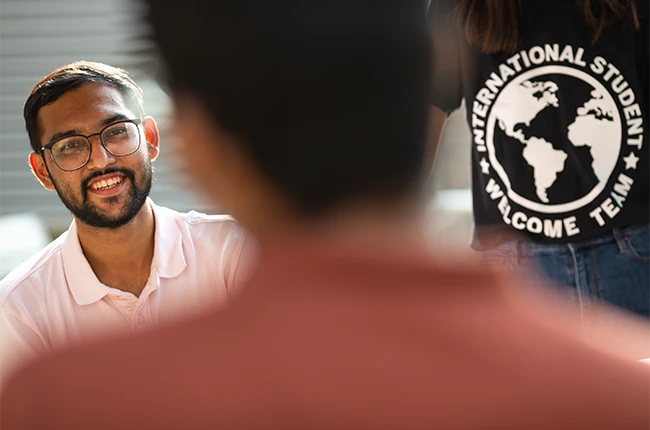 A person smiling and the back of a shirt that says International Student Welcome Team