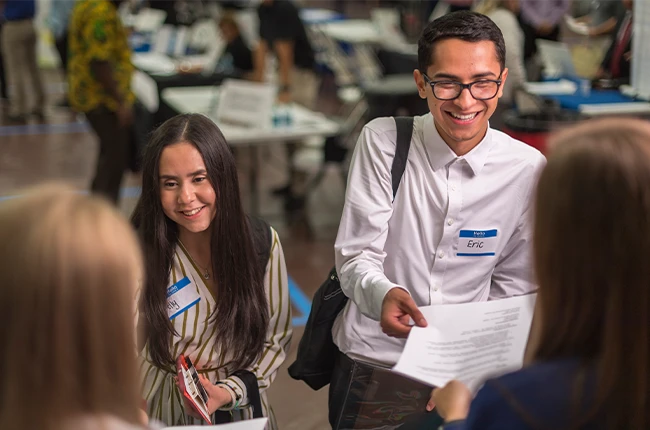 Two students handing their resumes out at a job fair