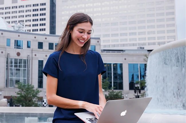 Student sitting in front of a fountain looking at a laptop