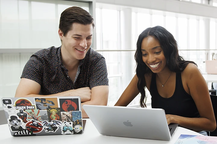 Two smiling students looking at laptops